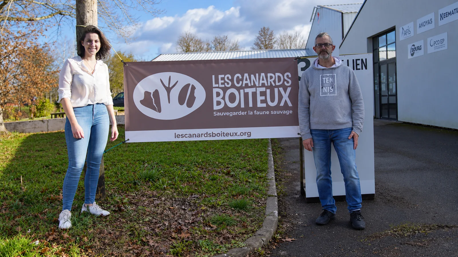 Deux personnes devant une banderole de l’Association Les Canards Boiteux